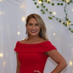 W&J junior Alyssa Pollice stands in front of while backdrop in red dress and smiles.