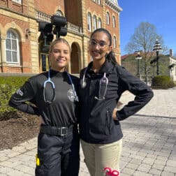 Photo of seniors Bianca Pate and Piper Scarry in their EMT apparel in front of Old Main.