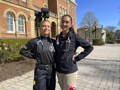 Photo of seniors Bianca Pate and Piper Scarry in their EMT apparel in front of Old Main.