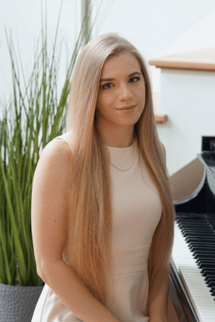W&J alumna Caroline Fedor '20 sit on a piano bench and smiles.