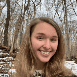 W&J junior Holly Troesch smiles in front of a wooded backdrop.