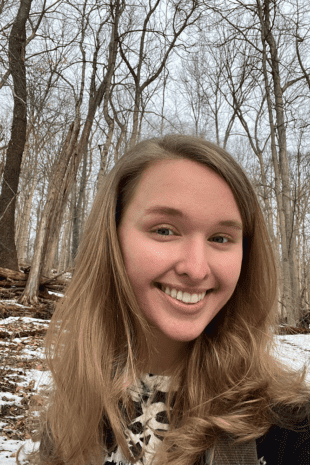 W&J junior Holly Troesch smiles in front of a wooded backdrop.