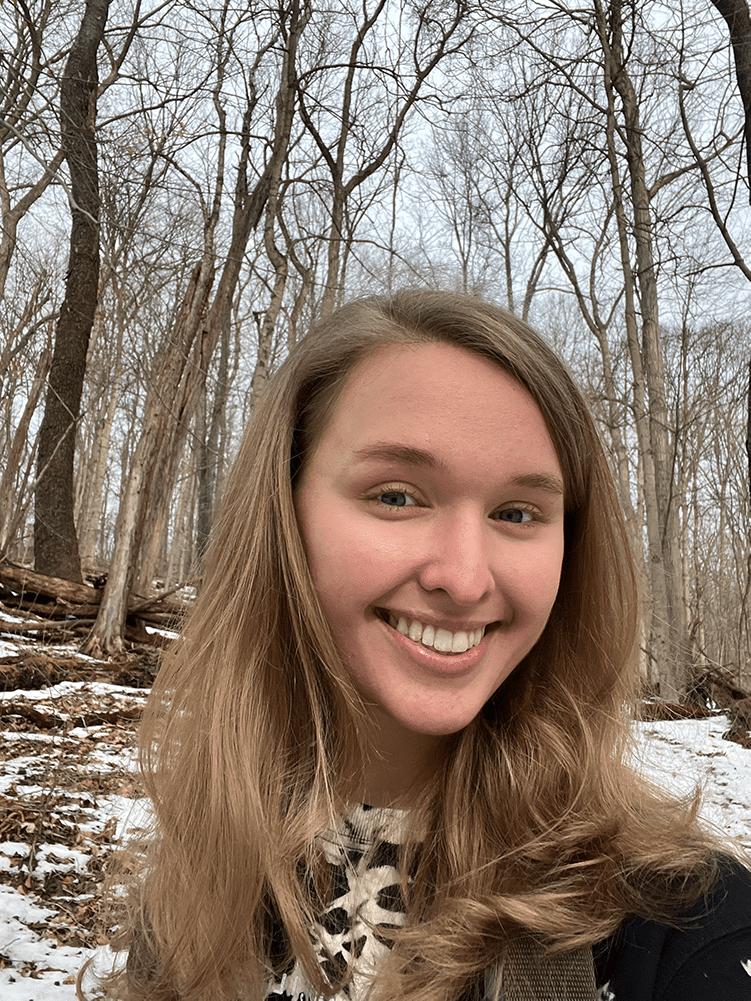 W&J junior Holly Troesch smiles in front of a wooded backdrop.