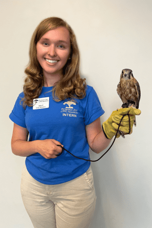 Rising senior Holly Troesch stands in blue, Pittsburgh Zoo & PPG Aquarium shirt and holds a small owl.