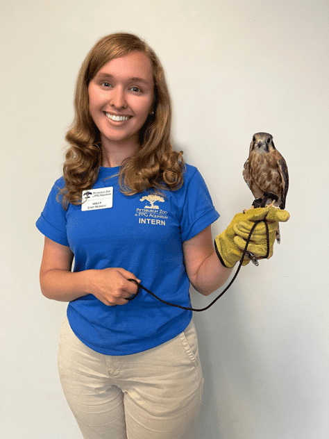 Rising senior Holly Troesch stands in blue, Pittsburgh Zoo & PPG Aquarium shirt and holds a small owl.