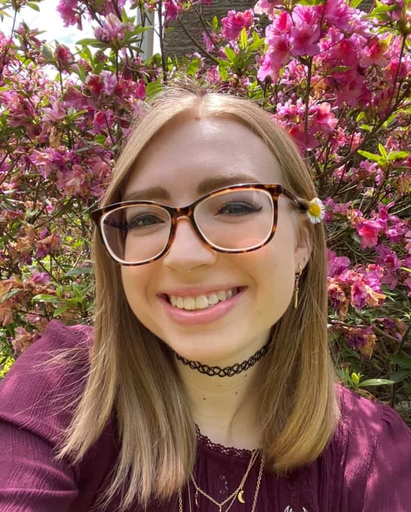 W&J senior Isabell Kratz smiles in front of pick flowers.