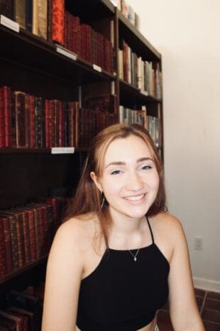 W&J senior Lily Bonasso sits in front of a bookcase and smiles.