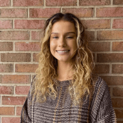 W&J Senior Rebecca Valencia smiles against a brick wall backdrop.