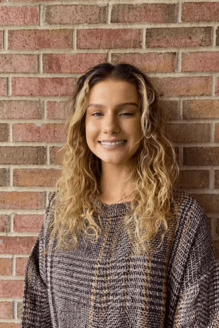 W&J Senior Rebecca Valencia smiles against a brick wall backdrop.