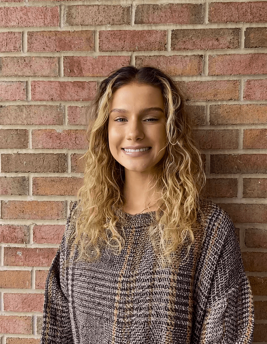 W&J Senior Rebecca Valencia smiles against a brick wall backdrop.