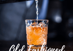 Hand and shaker pouring Old Fashioned cocktail