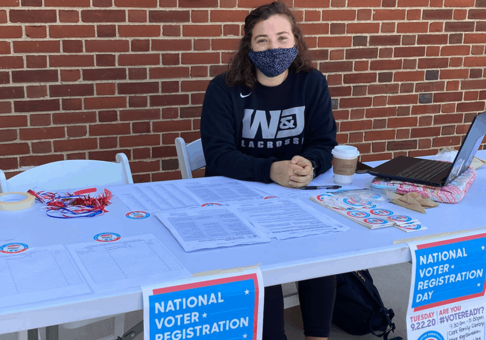 A student volunteer with the Student Voting Coalition sits at a table outside of Clark Family Library with voter registration materials.