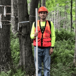 Brandon Marcucci '21 stands among trees in the Allegheny National Forest with gear to measure tree plots.