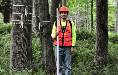 Brandon Marcucci '21 stands among trees in the Allegheny National Forest with gear to measure tree plots.