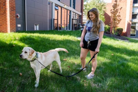 Photo of Dina Abbasian standing outside of the pet-friendly residence halls with her dog, Cecil.
