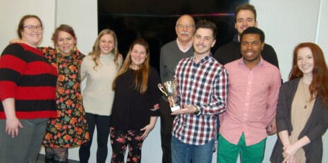 Students in the PrezTech Challenge winning class on Audio/Radio/Podcasting pose in the library classroom with their trophy.