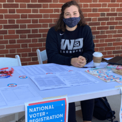 A student volunteer with the Student Voting Coalition sits at a table outside of Clark Family Library with voter registration materials.