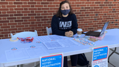 A student volunteer with the Student Voting Coalition sits at a table outside of Clark Family Library with voter registration materials.